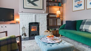 Una sala de estar acogedora con una chimenea blanca, un sofá verde, un televisor y una estantería.