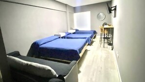 Una habitación con tres camas individuales, una pequeña mesa y sillas, y un ventanal.
