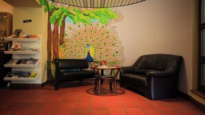 A lobby with a peacock mural, a black leather sofa, a small round table, and a bookshelf with magazines. - BOLA Kulturhostel (Bochum)