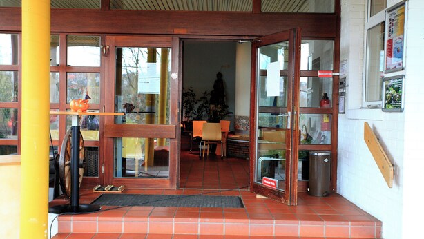 A restaurant entrance with a wooden interior, a yellow pillar, and a tiled floor. - BOLA Kulturhostel (Bochum)