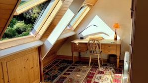 A cozy attic bedroom with a sloped ceiling, wooden walls, a desk with a lamp, and a colorful rug. - Les oliviers room, quiet and bright (Fouesnant)