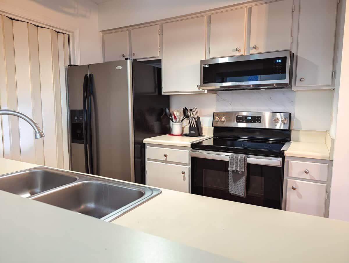 A modern kitchen with stainless steel appliances, a double sink, and white cabinetry.