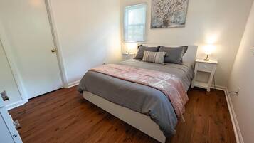 A bedroom with a bed, bedside tables, a window with blinds, and a painting on the wall.