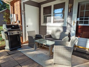 Une terrasse extérieure avec un barbecue, des meubles en osier et une table en verre.