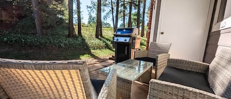 An outdoor patio with wicker furniture, a grill, and a view of trees.