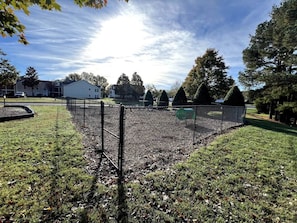 A fenced outdoor area with a grassy field, a metal fence, and a building in the background. - Stylish One-Level Near RDU | Cozy & Modern (Morrisville)