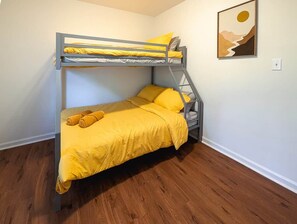 Una cama litera con colcha y almohadas amarillas, suelo de madera y un cuadro en la pared.
