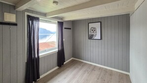 Una habitación con piso de madera, paredes grises, una ventana con cortinas y un cuadro enmarcado en la pared.