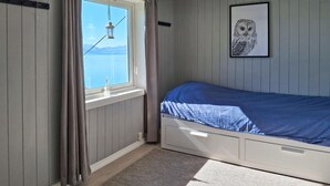 Un dormitorio con cama, ventana con cortinas, una lámpara colgante y un cuadro de un búho en la pared.