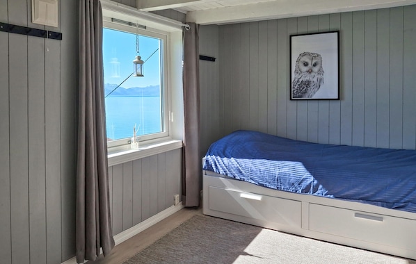 A bedroom with a bed, a window with curtains, a hanging lantern, and a framed owl picture on the wall.