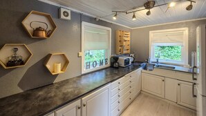 Una cocina moderna con armarios blancos, encimera negra y estantes de madera hexagonales. Se observa una ventana con vistas a zonas verdes.