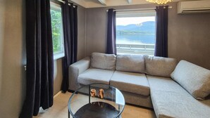 Una sala de estar moderna con un sofá grande, una mesa de centro de vidrio y vistas a un lago a través de ventanas amplias.