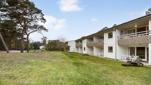 A modern building with multiple balconies, a grassy lawn, and trees in the background. - 1 bedroom lovely apartment in Nexø (Nexø)