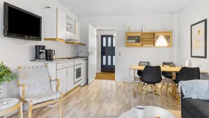 A modern kitchen with white cabinets, a coffee maker, and a TV. There is a dining area with a table and chairs. - 1 bedroom lovely apartment in Nexø (Nexø)