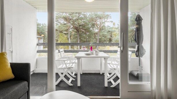 A balcony with a table and chairs, a yellow pillow, and a view of trees. - 1 bedroom lovely apartment in Nexø (Nexø)