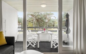 Een balkon met een tafel en stoelen, een geel kussen en uitzicht op bomen.