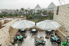 An outdoor dining area with tables and chairs, umbrellas, and a view of the pyramids. - Night Pyramids Inn (Giza)