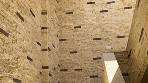 Eine Reihe Steinstufen führt zu einer Treppe vor einer Wand mit Steinmuster.