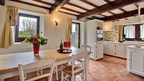 A dining area with a table set for four, a kitchen with white cabinets, and a stone wall.