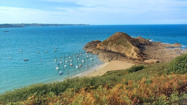 A coastal landscape with a rocky beach, clear blue sea, and boats anchored near the shore.