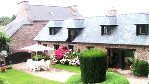 A stone building with a sloped roof, a patio with white chairs, and a well-maintained garden.