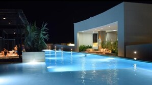 A swimming pool with a modern design, surrounded by lounge areas and a building with large windows. - Exclusive Ocean View Apartment - Reserva del Mar (Santa Marta)