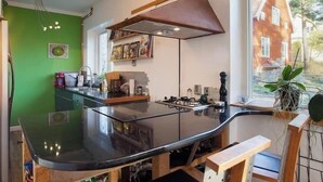 Una cocina moderna con una encimera negra curva, taburetes de madera, una lámpara colgante y vistas de una casa de ladrillo rojo a través de la ventana.
