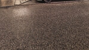 Vista de la calle con un coche plateado estacionado, un café llamado 'Melles' con mesas al aire libre y un edificio con el letrero 'Naprapatklinikk'.