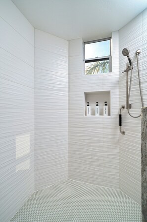 A modern shower area with a built-in shelf for toiletries, a handheld showerhead, and a rain shower attachment.