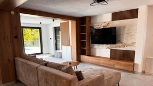 Una sala de estar moderna con un sofá seccional, un televisor montado en una pared de mármol y un mueble de entretenimiento de madera.