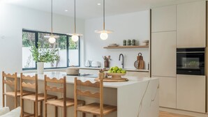 Una cocina moderna con una isla central, sillas de madera, luces colgantes y vistas al exterior.