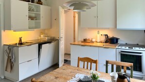 Une cuisine de taille réduite avec des meubles blancs, une table à manger en bois et une cuisinière.