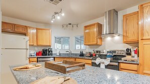 A modern kitchen with granite countertops, wooden cabinets, stainless steel appliances, and a central island with a cutting board and towels.
