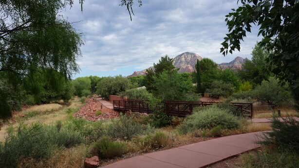 A paved pathway with benches, surrounded by greenery and a mountain backdrop.