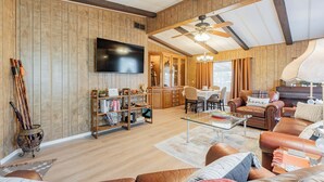 A spacious living room with wooden walls, a ceiling fan, a flat-screen TV, and a dining area with a table and chairs.
