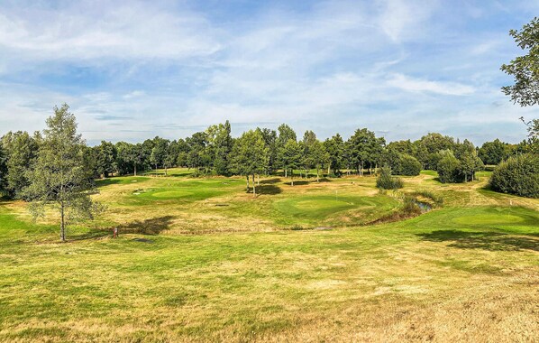A golf course with well-maintained grass, trees, and a clear sky.