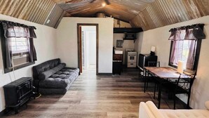 Ett kompakt och rustikt rum med en sovplats på ett loft, en soffa, ett matbord och ett litet kök.