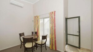 A small dining area with a round table and four chairs, a sliding glass door with colorful curtains, and a door with a metal frame. - Walmsley Motor Lodge (Auckland)