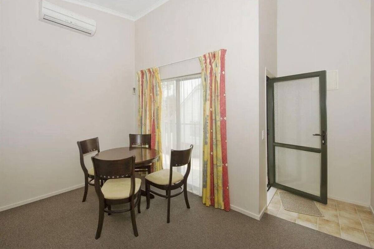 A small dining area with a round table and four chairs, a sliding glass door with colorful curtains, and a door with a metal frame.