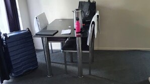 A small, simple room with a table, a chair, a suitcase, and a bag. - Walmsley Motor Lodge (Auckland)