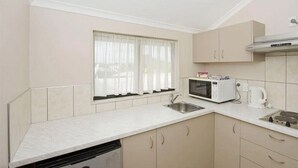 A compact kitchen with a microwave, kettle, and sink. - Walmsley Motor Lodge (Auckland)