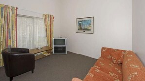 A room with a sofa, a chair, a television, and a window with curtains. - Walmsley Motor Lodge (Auckland)