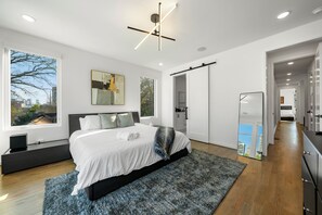 Ein modernes Schlafzimmer mit einem großen Bett, Blick auf die Stadt durch das Fenster und einer außergew öhnlichen Deckenleuchte.