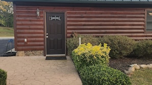 Une cabane en rondins avec un toit en métal, une porte en bois sombre et une allée dallée.