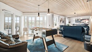 A spacious living area with a foosball table, a blue sofa, and a television mounted on the wall. - Awesome home in Ringkøbing with sauna (Ringkøbing)