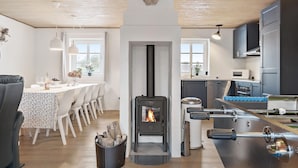 A modern kitchen with a wood-burning stove, a dining area with a white table and chairs, and a kitchen island with a sink and appliances. - Awesome home in Ringkøbing with sauna (Ringkøbing)