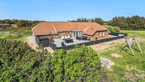 A two-story house with a tiled roof, a patio with outdoor furniture, and a fenced yard. - Awesome home in Ringkøbing with sauna (Ringkøbing)