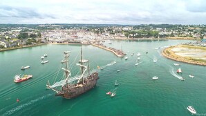 A harbor with a large ship docked, surrounded by smaller boats and a town in the background. - Gîte de Kerberso near Paimpol in Côtes-d'Armor (Pléhédel)