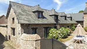 A stone building with a sloped roof, a gated entrance, and a small patio with outdoor furniture. - Gîte de Kerberso near Paimpol in Côtes-d'Armor (Pléhédel)