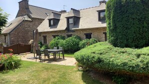 A stone house with a sloped roof, a patio with a table and chairs, and well-maintained hedges. - Gîte de Kerberso near Paimpol in Côtes-d'Armor (Pléhédel)